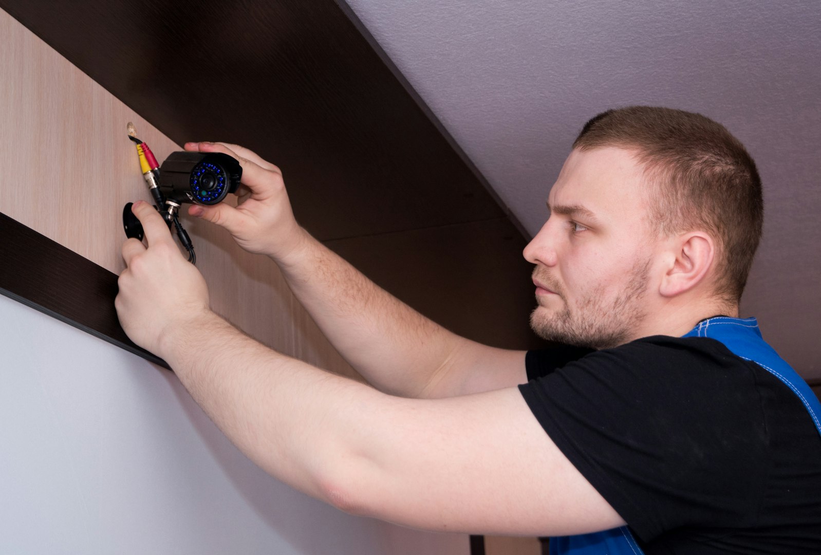 Man on a ladder using a screwdriver to install a modern pendant light fixture on a ceiling in a contemporary home interior. Focus on lighting installation, home maintenance and professional handiwork with visible tools, wiring and three hanging pendant lamps over a kitchen or living area.